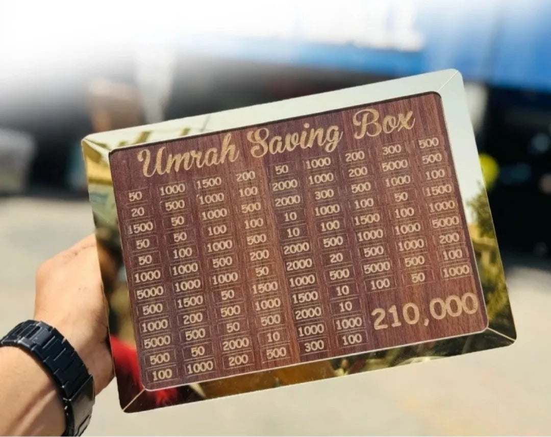 Gold 'Umrah Saving Box' with displayed, held by a hand.